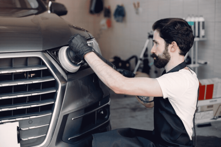 A man is polishing the hood of a car in a garage.